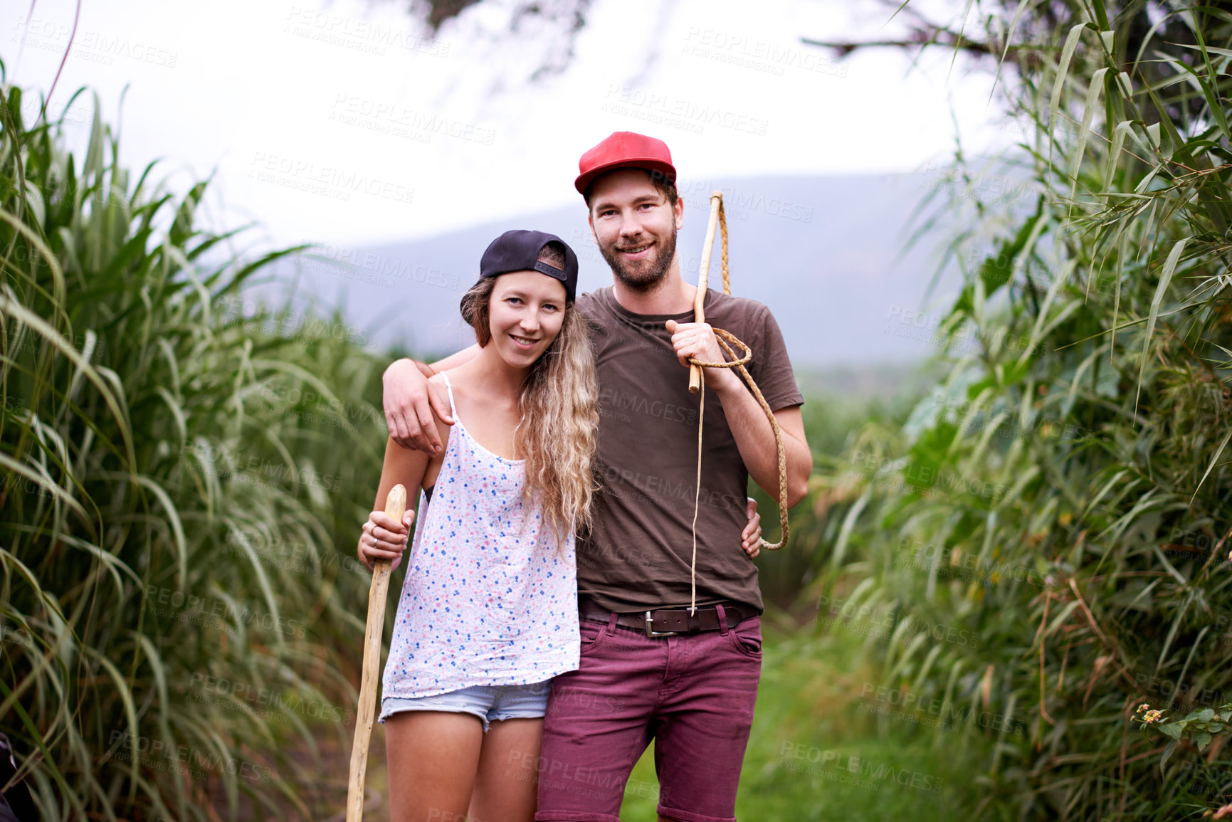 Buy stock photo Happy couple, portrait and hiking in nature with stick for travel, adventure or embrace for love in countryside farm. Man, woman or trekking in field together on holiday, tourism or explore Australia