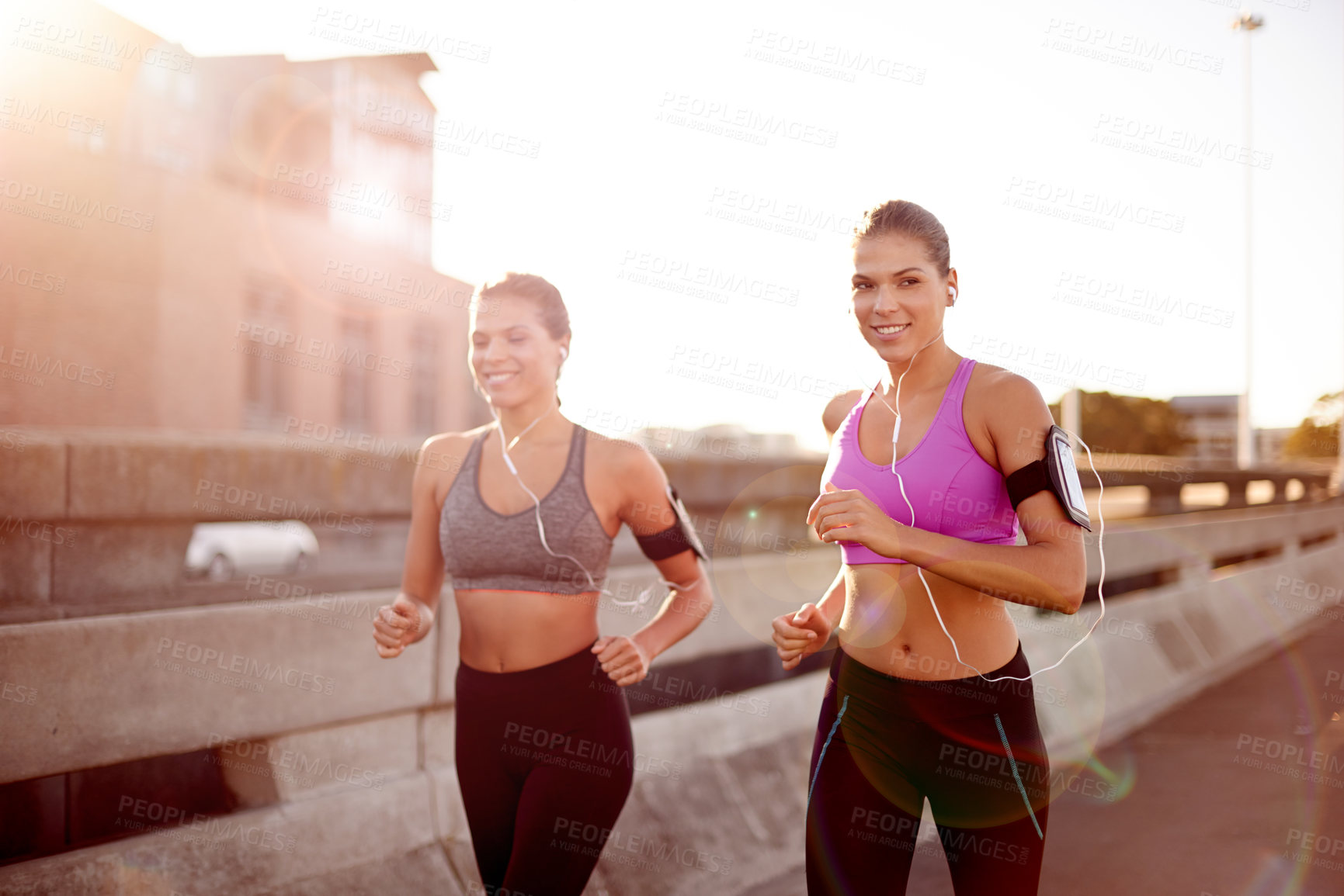 Buy stock photo Women, running and together in street with earphones, training or wearable tech for audio in city. People, twins and sisters for exercise, streaming or cardio workout on bridge with portrait in Spain