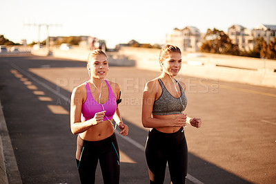 Buy stock photo Women, fitness and bridge for running in city, streaming music and team support with twin exercise. Urban, workout together and podcast for cardio sports, marathon training and earphones for sound