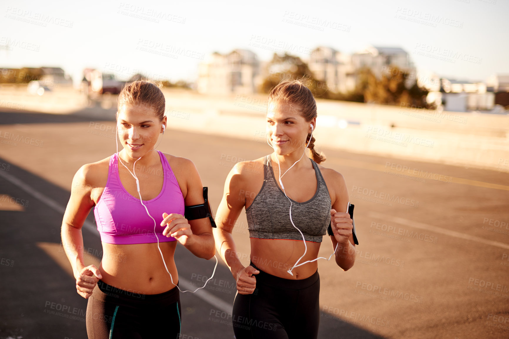 Buy stock photo Women, exercise and outdoor for running in city, streaming song and team support with fitness. Urban town, workout together and podcast for cardio sports, marathon training and earphones for twins