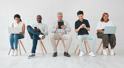 Buy stock photo Shot of a diverse group of people using digital devices while sitting in line against a white background