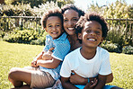 Adorable african american boys sitting on their mother's lap outside. Carefree african american family spending time outdoors at the park or their backyard. Mom embracing two sons 