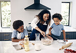 Adorable little boy with afro baking in the kitchen at home with his mom and brother. Cheerful mixed race woman mixing ingredients with the help of her little boys. Baking is a bonding activity