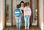 Young mother seeing her kids off to school. Mixed race saying goodbye to her son and daughter as they leave home for school. Happy mom greeting her children at the front door of their house