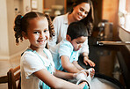 Happy cheerful little mixed race girl helping her mother wash the dishes in the kitchen at home. Hispanic child smiling while washing a cup with soap and water. Family keeping their house clean
