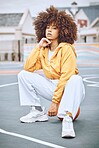 Trendy, stylish and fashionable female basketball player sitting on a ball at the court against an urban background. Young, edgy and serious woman with an afro posing outside in the city in the day