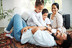 Closeup of a young hispanic family playing together on the lounge floor at home. Mixed race father and mother having fun while playing with their cute little son and daughter in the lounge at home