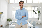 Young happy caucasian businessman standing with his arms crossed while in an office alone. One confident male boss standing at work