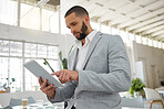 Young focused mixed race businessman working on a digital tablet in an office. One hispanic male boss holding using social media on a digital tablet at work