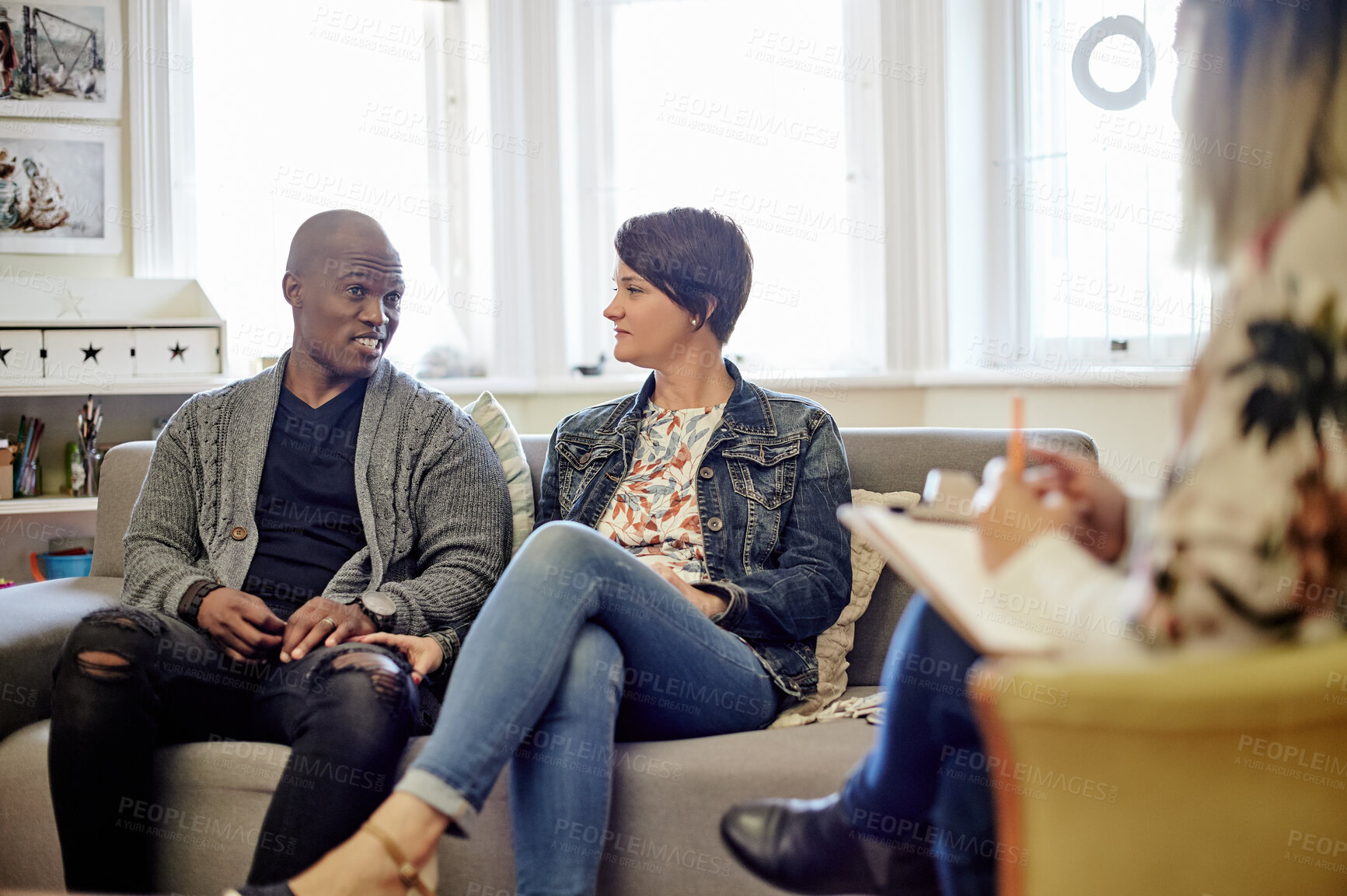 Buy stock photo Psychology, sofa and couple talking to a therapist in her modern office at counseling clinic. Discussion, therapy session and interracial man and woman on couch speaking to relationship psychologist.