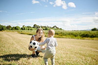 Buy stock photo Baby, soccer ball and a mother playing with her son on a field while bonding together during summer. Kids, love a young woman having fun with her young male child using sports on green grass outside