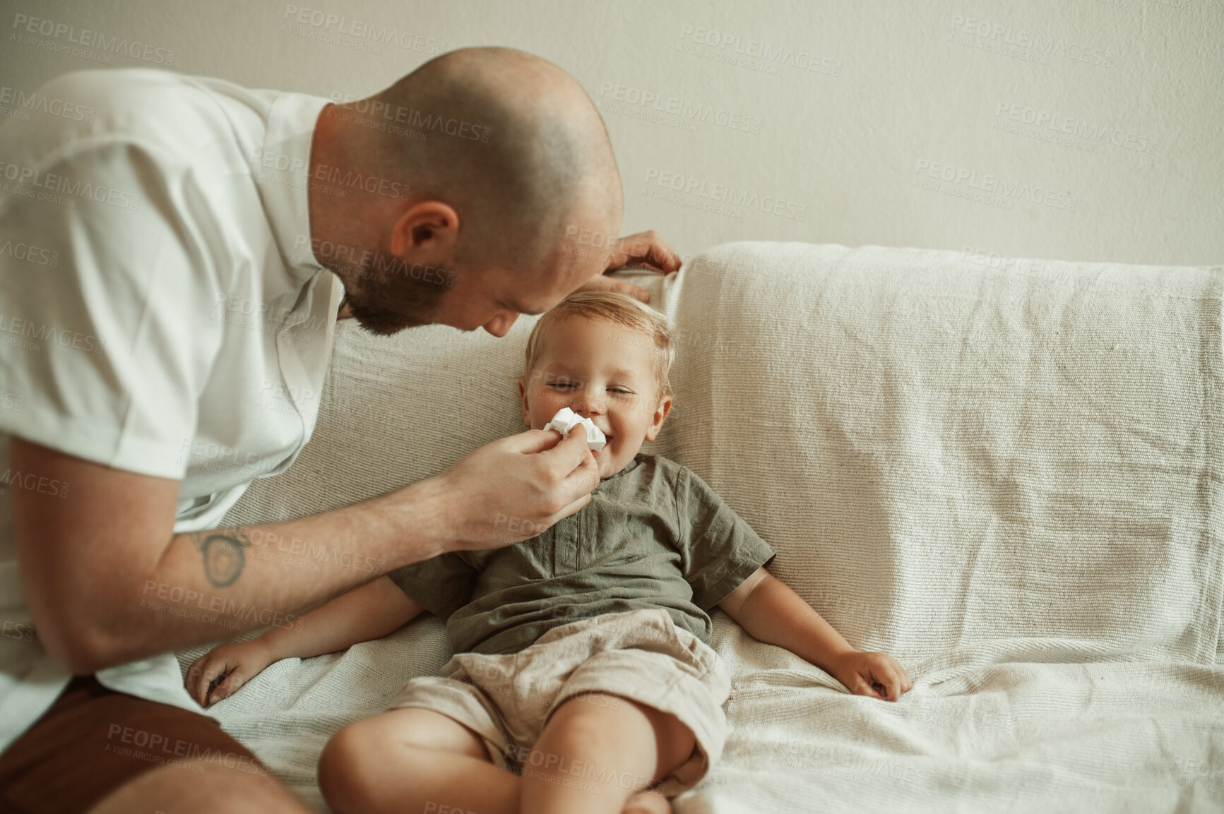 Buy stock photo Dad, child and wipe nose of sick kid on sofa in home living room, happy and smile for care. Father, boy and toddler with tissue for flu, allergies or covid, virus or disease, illness or cold in house