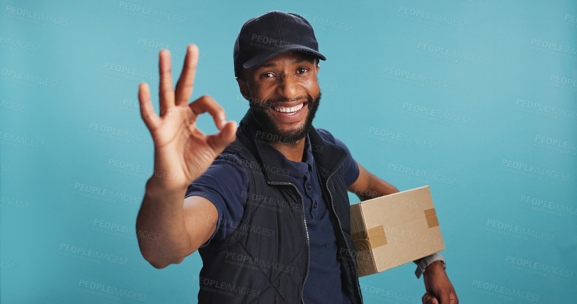 Buy stock photo Portrait, box and delivery man with ok sign in studio for ecommerce, perfect order or logistic. African courier, smile or okay hand gesture for quality service, shipping or package on blue background