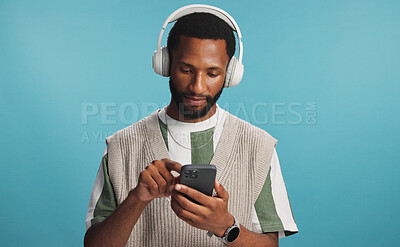 Buy stock photo Headphones, phone and black man in studio with music, playlist or album for review on blog. Type, audio tech and African male influencer listening to song online for streaming app by blue background