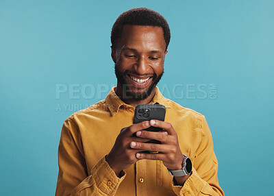 Buy stock photo Black man, phone and happy with typing in studio for text message, internet search or playing online games. Mockup space, person and smile with smartphone for communication or chat on blue background