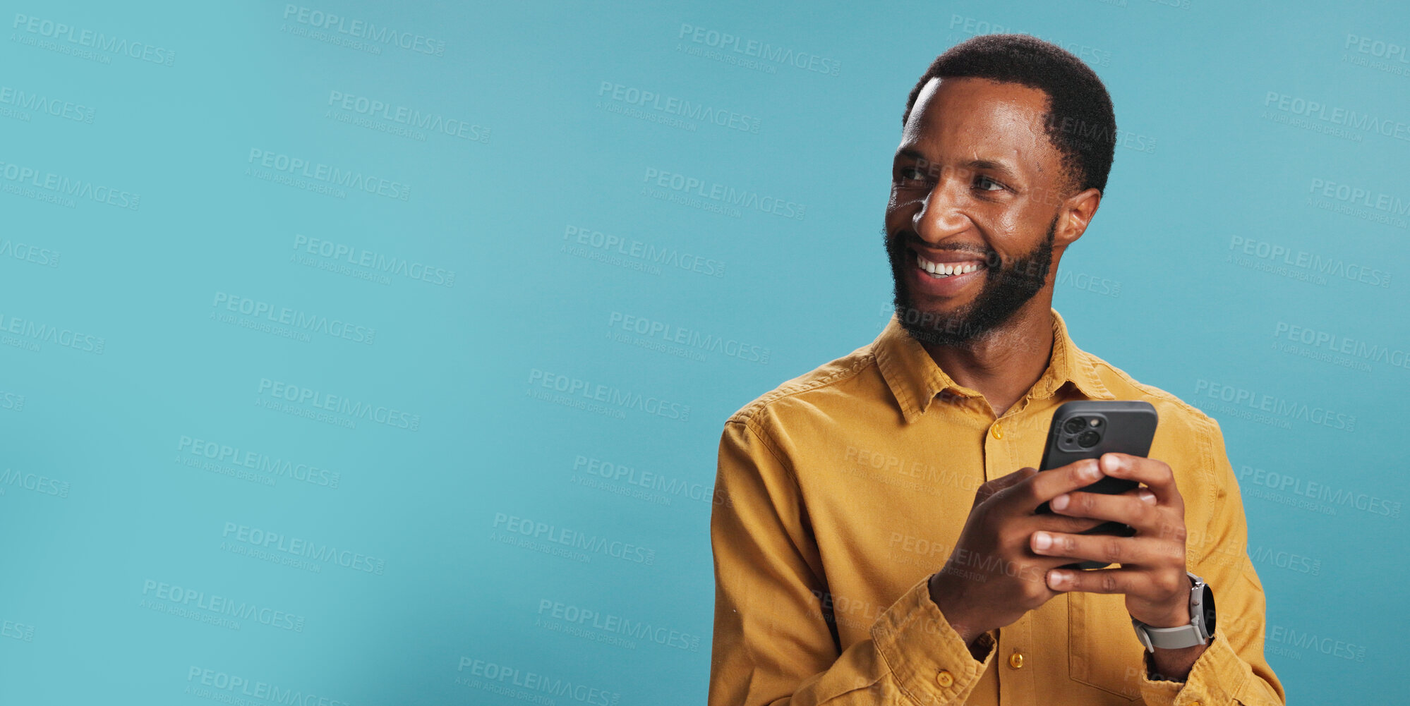 Buy stock photo Black man, thinking and smile with phone in studio for text message response, email feedback or search ideas. Mockup space, person and happy with smartphone for networking or chat on blue background