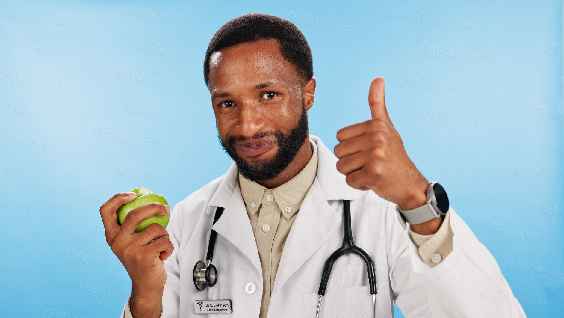 Buy stock photo Thumbs up, black man or doctor eating apple in portrait for fibre, healthcare advice or healthy food choice. Studio, blue background and African nutritionist with fruit for approval and vitamin c