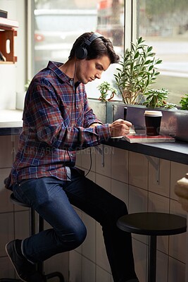 Buy stock photo Man, writing and notebook with headphones in coffee shop for remote work, planning or schedule. Person, journalist or writer with book, streaming or music subscription with review for article in cafe