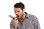 Man, angry and shout on phone call in studio with stress, voice and mental health by white background. Person, smartphone and loudspeaker for contact, frustrated and screaming on mobile network