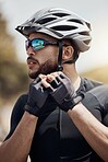 Closeup of male cyclist wearing glasses and gloves while tying or removing his cycling helmet. Athletic young man putting on a helmet for safety. Professional cyclist getting ready for a ride or training outdoors