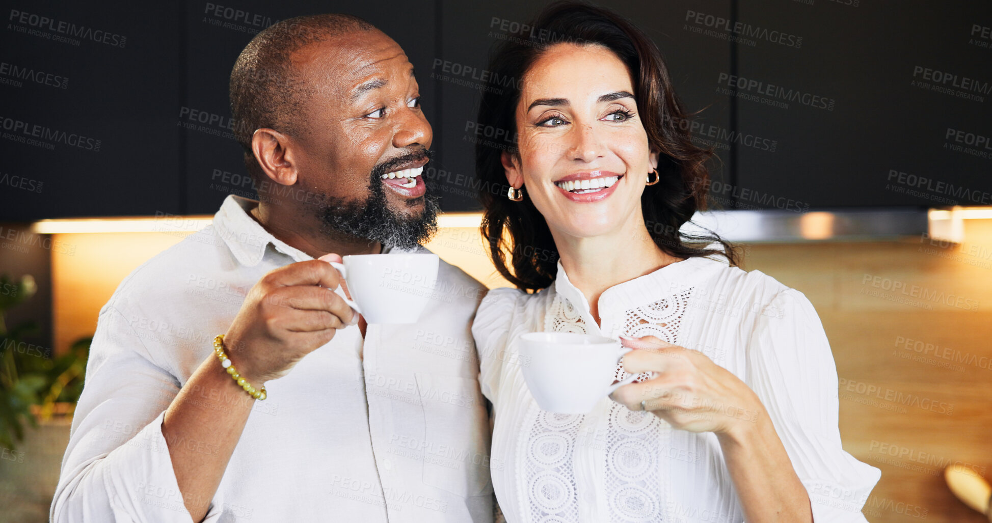 Buy stock photo Happy, interracial and couple with coffee in kitchen for caffeine start, morning routine and bonding together. Mature, people and warm beverage with laughing, funny discussion and commitment at house