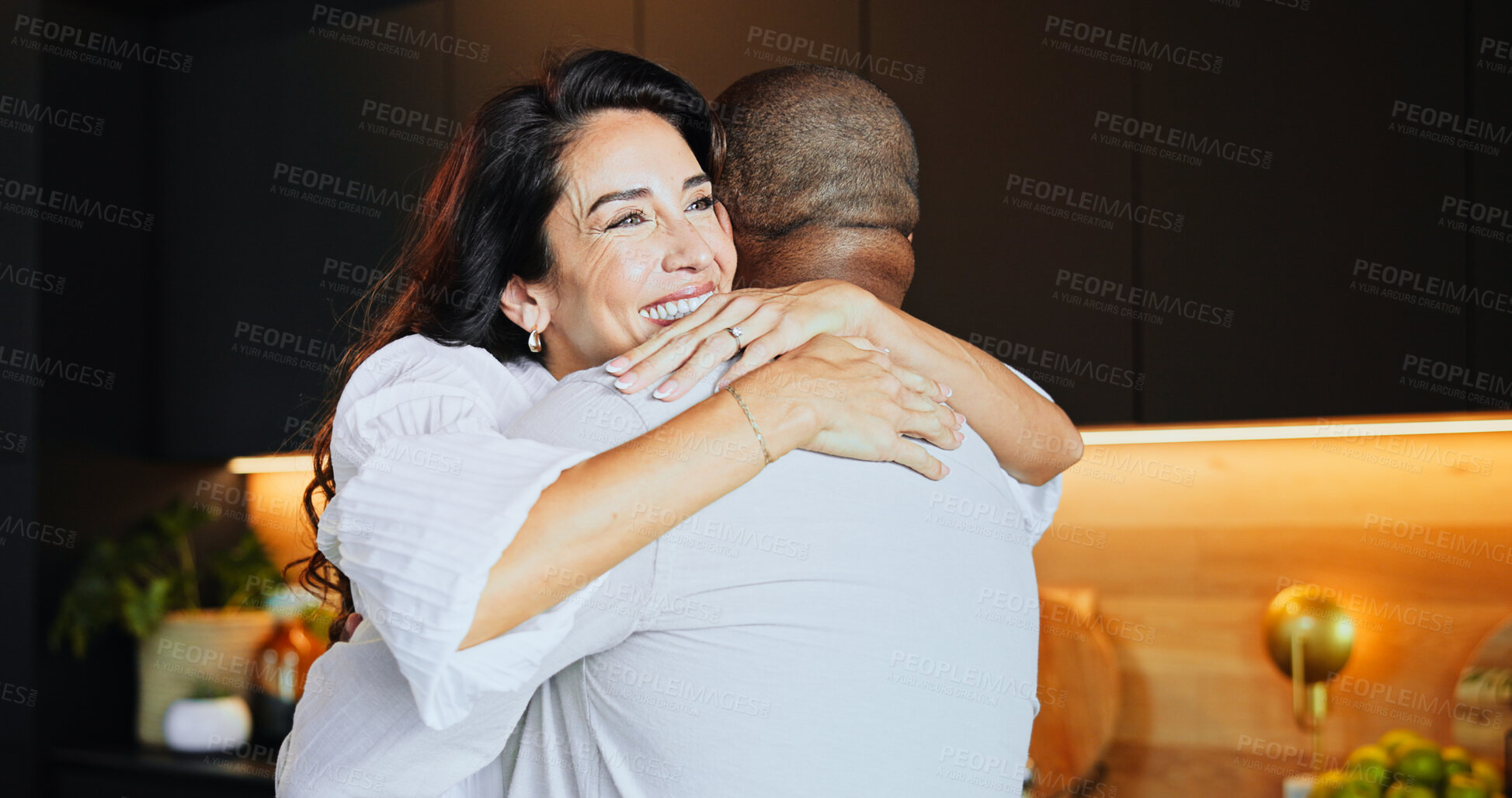 Buy stock photo Hug, smile and mature interracial couple in kitchen with home, bonding and marriage or romance. Safety, security and trust with man, woman and embrace in modern apartment for anniversary celebration