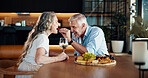 Love, feeding and mature couple in kitchen in home with charcuterie board for date together. Romantic, happy and man eating snack platter with woman for marriage anniversary celebration at house.