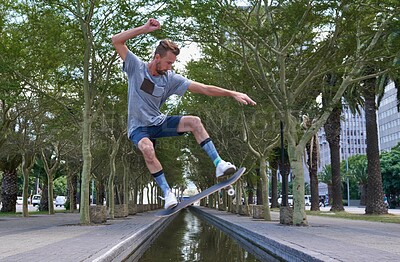 Buy stock photo Skateboard, jump and water with man in city for culture, extreme sports and trick flip. Fitness, hobby and street with person and training at canal for skating skill, energy and balance practice