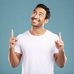 Handsome young mixed race man pointing towards copyspace while standing in studio isolated against a blue background. Happy hispanic male advertising or endorsing your product, company or idea