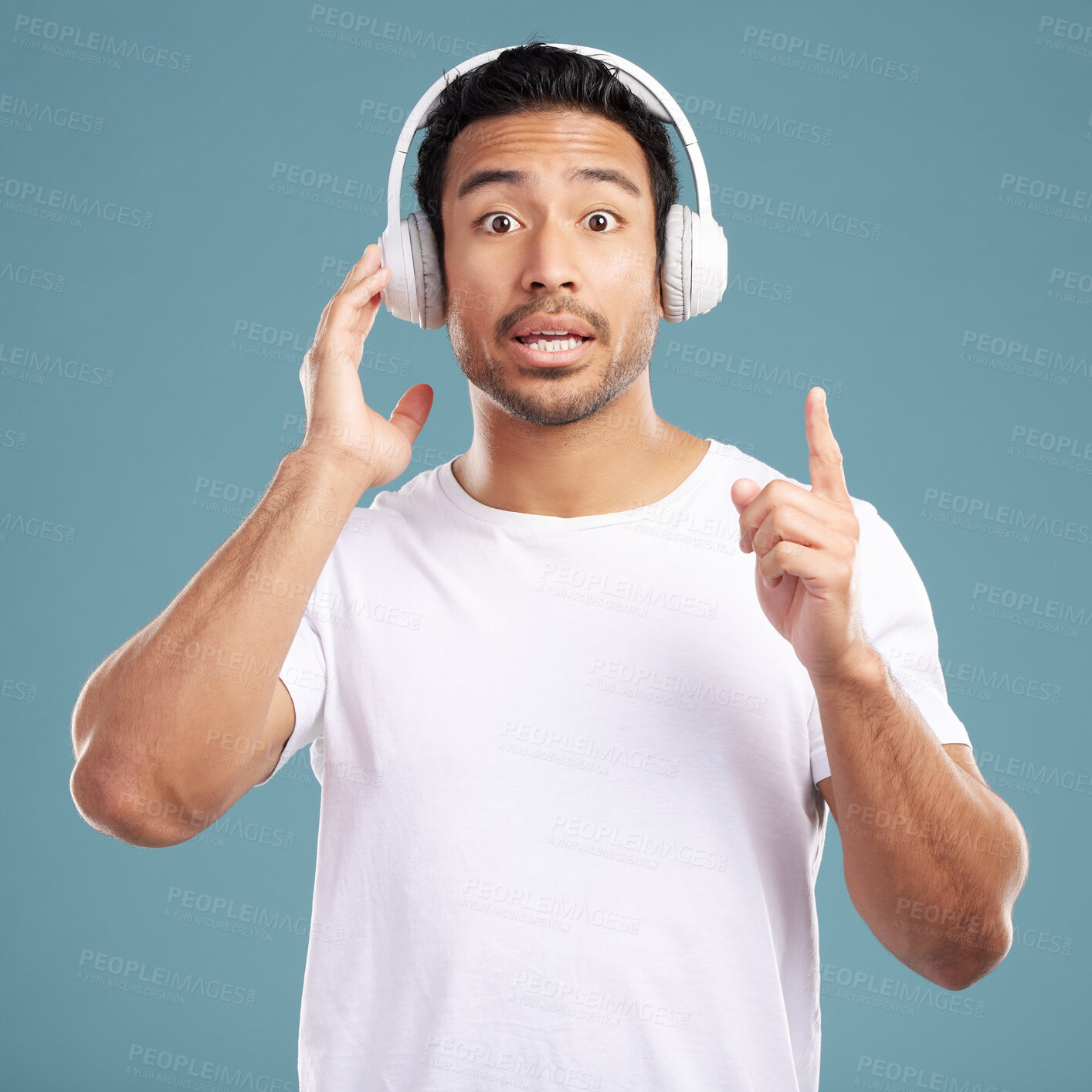 Buy stock photo Portrait, surprise and man in studio, headphones and listening to music on blue background. Japanese person, model and guy with headset, shocked and expression with wow and announcement on radio