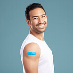 Handsome young mixed race man showing off his covid 19 jab while standing in studio isolated against a blue background. Hispanic male with a plaster on his corona virus vaccination injection site