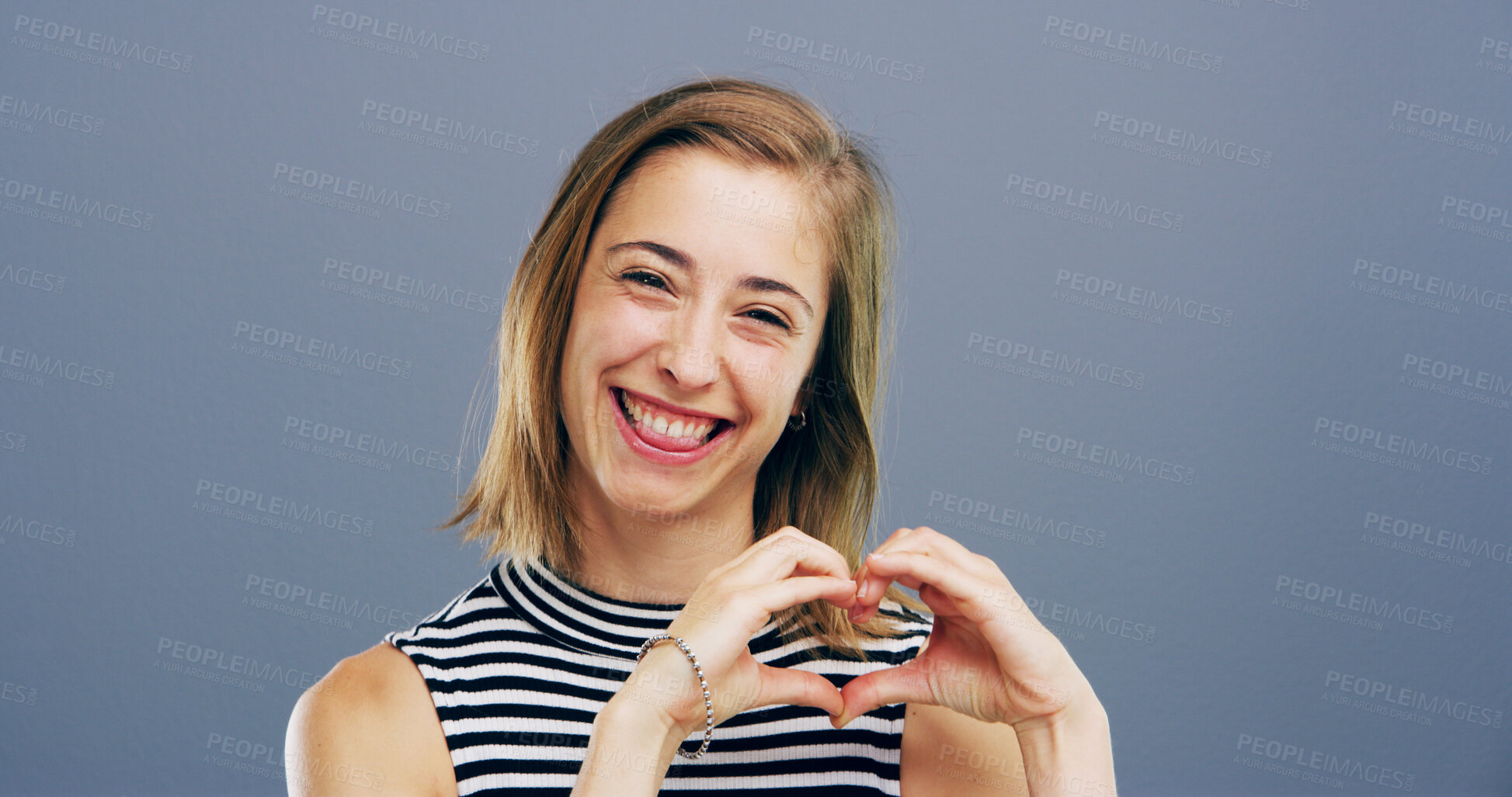 Buy stock photo Happy, portrait and girl with heart hands in studio for flirting, romance and appreciation. Space, tongue out and love gesture on gray background for support, gratitude and affection sign with smile