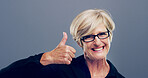 Mature, happy woman and portrait with thumbs up for feedback, opinion or good job on a gray background. Female person, glasses or model with like emoji or yes sign in studio for positive approval