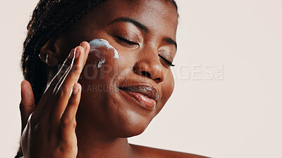 Buy stock photo Happy, black woman and lotion on face in studio for facial hydration, treatment and sunscreen protection. Female person, apply cream and spf cosmetics for dermatology, anti aging and white background