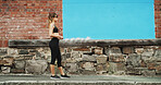 Girl, city and runner with earphones by wall, space and streaming with sound, subscription and exercise. Woman, audio tech and profile with music with fitness, training and workout on road in Italy