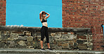 Woman, runner and tired in city by wall, space and earphones for streaming subscription, sound or exercise. Girl, audio tech and listen to music with fitness, training or fatigue on sidewalk in Italy
