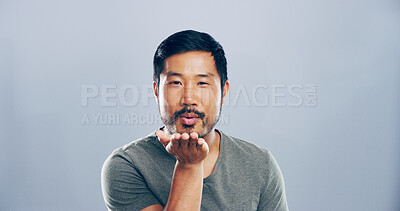 Buy stock photo Portrait, asian man and blowing kiss with romance for love, affection or greeting on a gray studio background. Creative, male person or model with care, palm or flirt in distance on mockup space