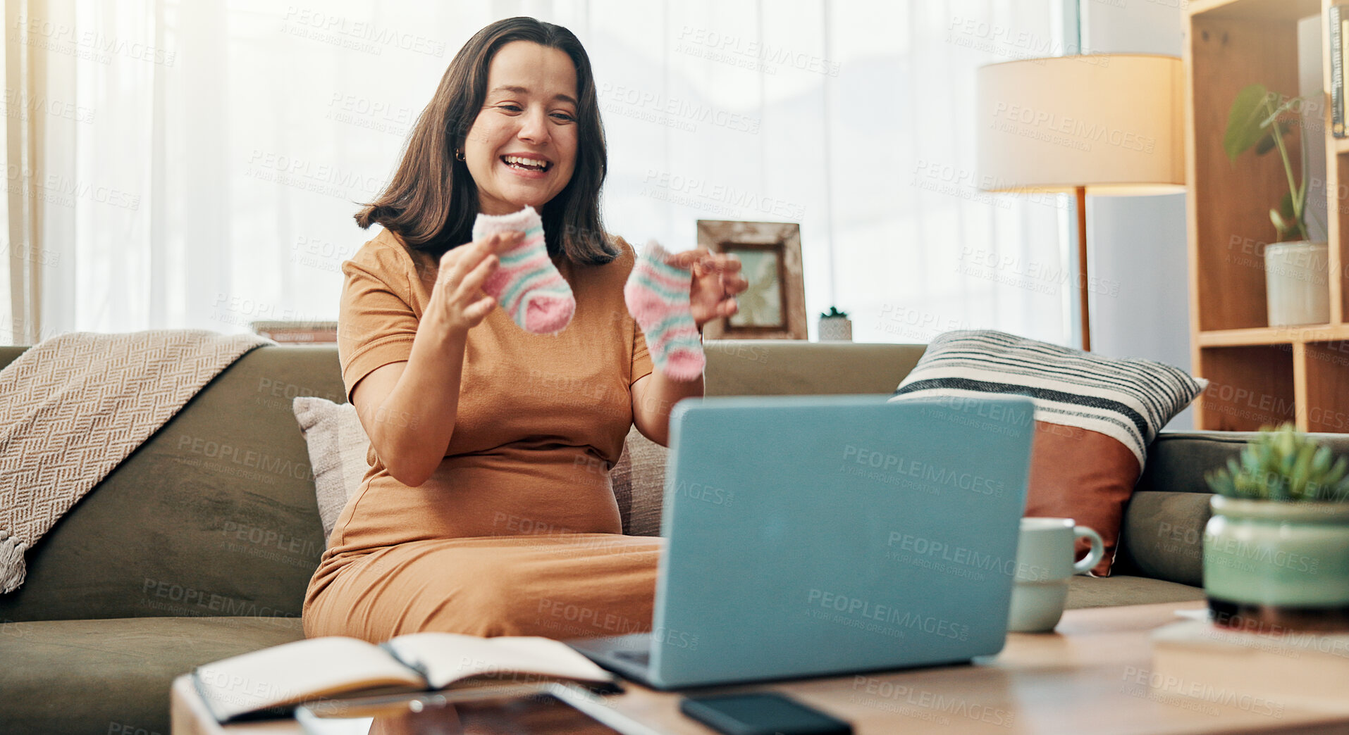 Buy stock photo Pregnant, woman and baby clothes for video call, smile and sharing motherhood on social media with laptop. House, influencer and socks for gender reveal on app, communication or preparation for child