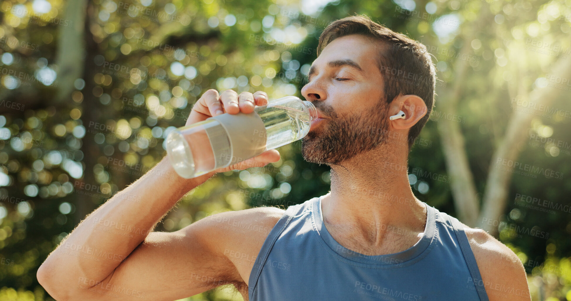 Buy stock photo Man, fitness and drinking water in park, break and earphones with streaming subscription in summer. Person, bottle and liquid for hydration, detox and wellness with exercise, workout and training