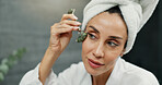 Face roller, skincare and woman in bathroom in home for natural, health and morning routine. Wellness, beauty and female person with jade stone facial tool for lymphatic drainage in apartment.