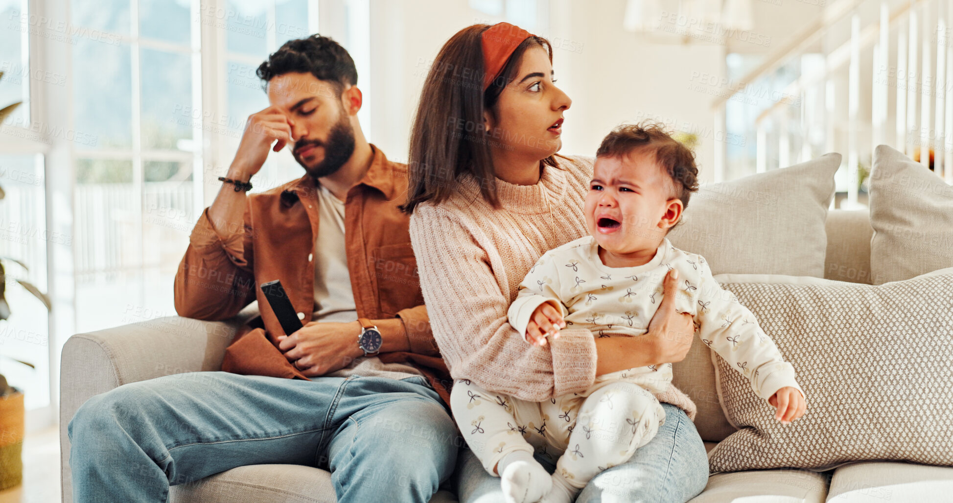 Buy stock photo Home, man and woman with baby, crying and stress for new parents with child, lounge and noise. Family, father and annoyed by interruption from game, thinking or mother with emotional toddler in house