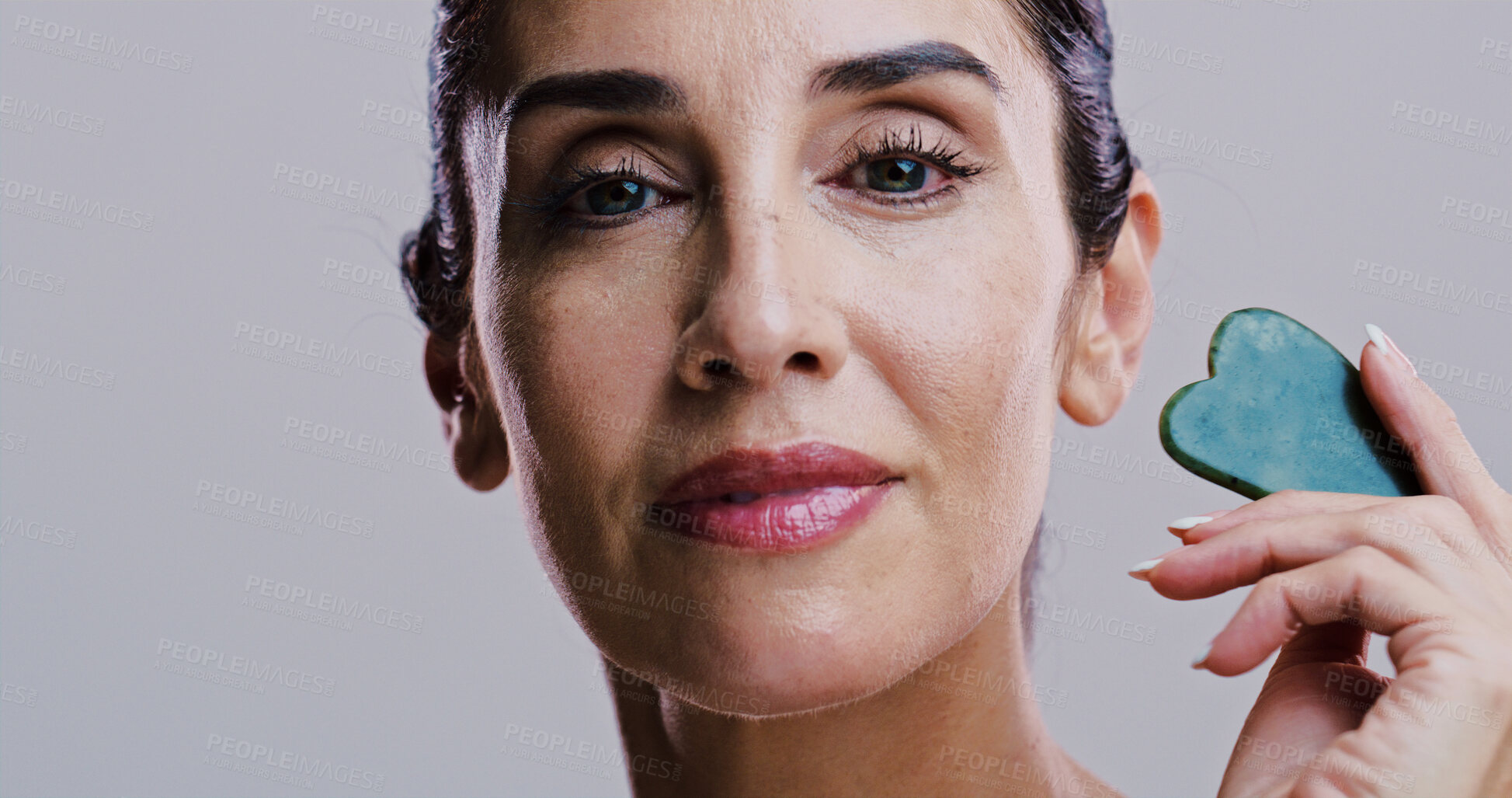 Buy stock photo Facial massage, portrait and skincare with woman in studio for antiaging cosmetics or dermatology. Beauty, gua sha and jade with person isolated on gray background for crystal stone face treatment