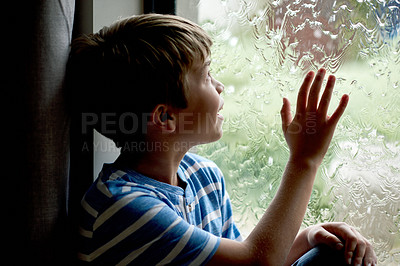 Buy stock photo Happy, kid and watching rain by window for sensory experience, imagination or playing with raindrops. Boy child, curious and thinking in home with daydreaming, checking scenery or winter weather view