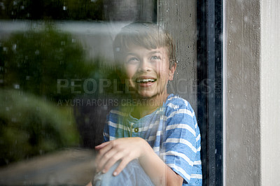 Buy stock photo Happy, child and rain by window in home for sensory experience, imagination and soothing sound. Boy kid, smile and curious in house with daydreaming, development and checking scenery with reflection