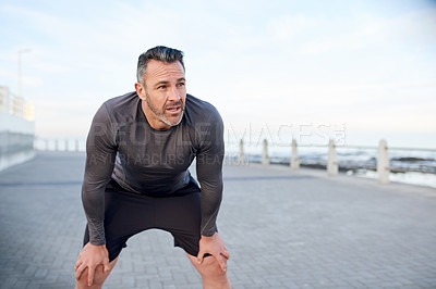 Buy stock photo Mature man, runner and tired on promenade by ocean, break or burnout with breathing for workout in morning. Person, training and outdoor by sea with fatigue, cramp or exhausted with exercise in Spain