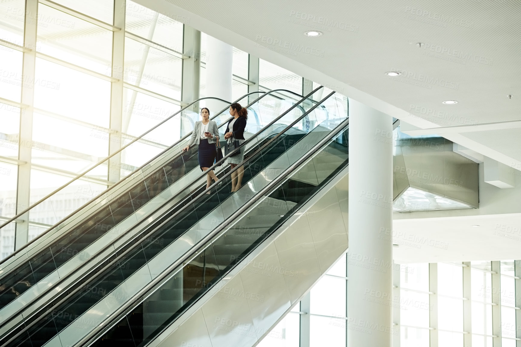 Buy stock photo Business, women or travel on escalator in office for meeting commute, work arrival or career discussion. Professional, people or talking on moving staircase for corporate journey or seminar departure
