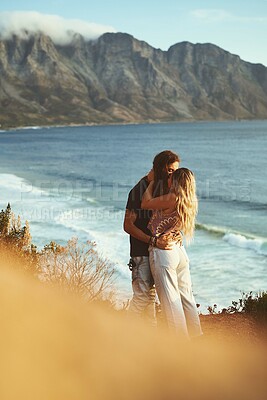Buy stock photo Ocean, mountain and couple with kiss on vacation, travel holiday and bonding together with embrace. Outdoor, man and woman with hug for anniversary, connection and adventure with affection by flare