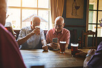 Two senior men sitting with friends and using a cellphone in a bar, bonding, senior friends browsing online, social media, social networking, drinking beer