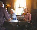 Senior man sitting with friends and drinking beer while reading a newspaper in a pub, elderly man browsing newspaper, drinking a pint of beer