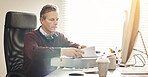 A businessman analysing paperwork and using a computer in a modern office. A mature male executive working online and going over a business document at his desk
